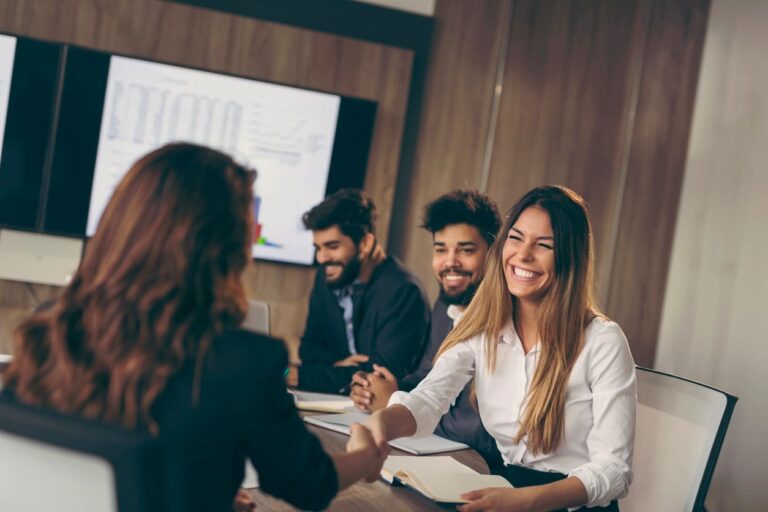 Business meeting with professionals smiling and shaking hands in a modern conference room.